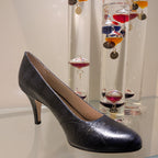 Kate Navy snakeskin-textured high-heeled pump shoe displayed on a glass shelf, with decorative glass vials in the background.