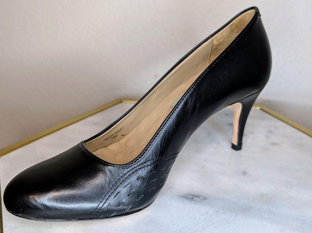 Salem black leather high-heeled pump shoe with a pointed toe and a slim stiletto heel, displayed on a white marble surface with a gold-framed edge against a neutral beige background.