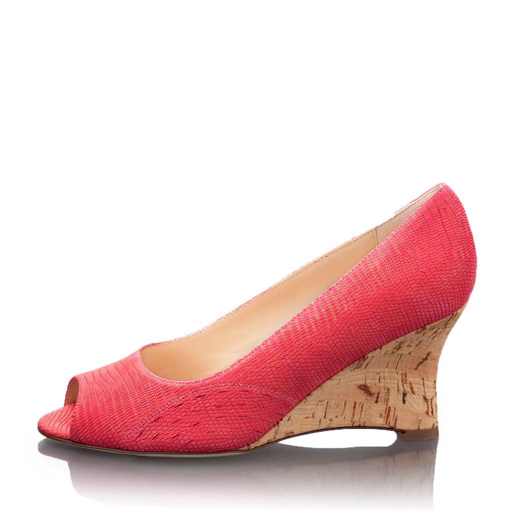 A single women's wedge pump in a bright coral raspberry (pink) textured fabric with an open toe and a natural cork wedge heel, shown on a white background with a faint reflection.